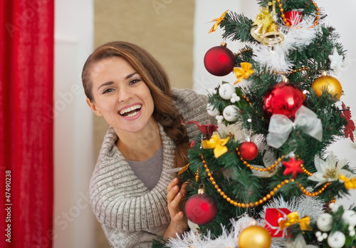 Photo: Happy young woman looking out from Christmas tree Happy young woman looking out from Christmas tree