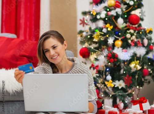 Photo: Happy young woman making online purchases near Christmas tree Happy young woman making online purchases near Christmas tree