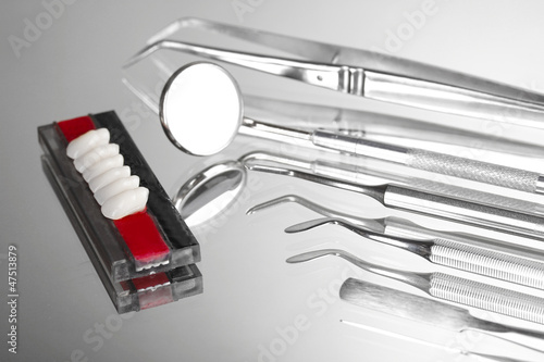 Photo: Set of dental tools with denture on grey background Set of dental tools with denture on grey background