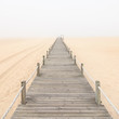 Wooden footbridge on a foggy sand beach background. Portugal.