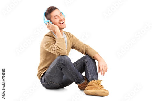 Photo: A young guy sitting on a floor and listening music on headphones A young guy sitting on a floor and listening music on headphones