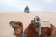 Male person sitting on sand in desert with camel on foreground