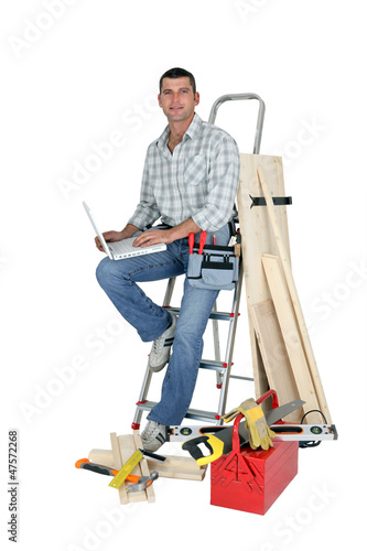 Photo: Handyman sitting on a ladder with laptop Handyman sitting on a ladder with laptop