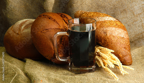 Photo: tankard of kvass and rye breads with ears, on burlap background tankard of kvass and rye breads with ears, on burlap background