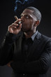 Black man wearing suit gangster style smoking cigar. Studio shot