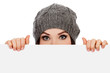 Photo: Girl in knitted hat looking over white board, white background Girl in knitted hat looking over white board, white background