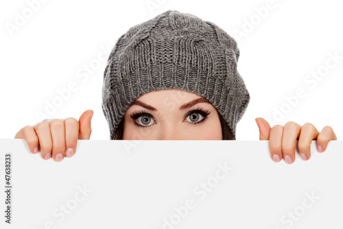 Photo: Girl in knitted hat looking over white board, white background Girl in knitted hat looking over white board, white background