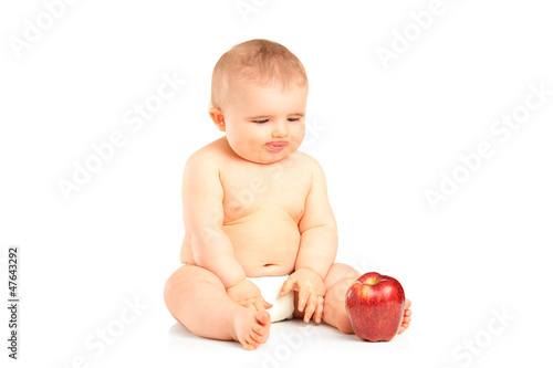 Photo: Baby boy sitting and looking at an apple Baby boy sitting and looking at an apple