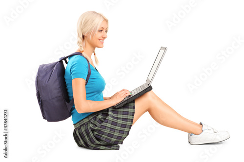 Photo: A smiling student working on a laptop and sitting on a floor A smiling student working on a laptop and sitting on a floor