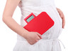 Belly of pregnant woman in white holding red balance isolated