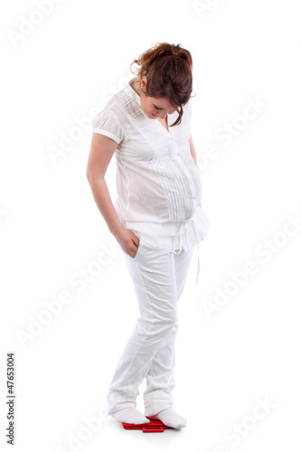 Photo: Pregnant woman in white stands on red balance and looks Pregnant woman in white stands on red balance and looks