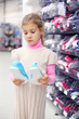 Pretty little girl considers gym shoes and stands near shelves