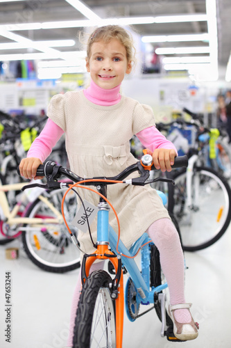 Photo: Smiling girl sits on bright bicycle and looks at camera Smiling girl sits on bright bicycle and looks at camera