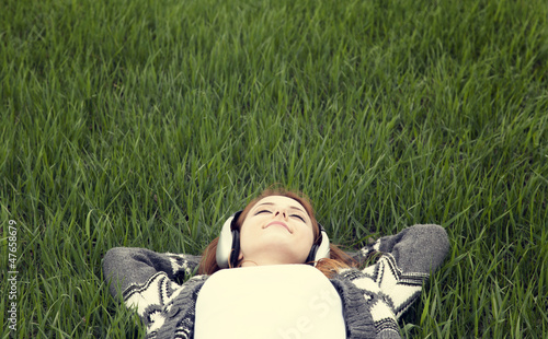 Photo: Young with headphones lying down at green grass. Young with headphones lying down at green grass.