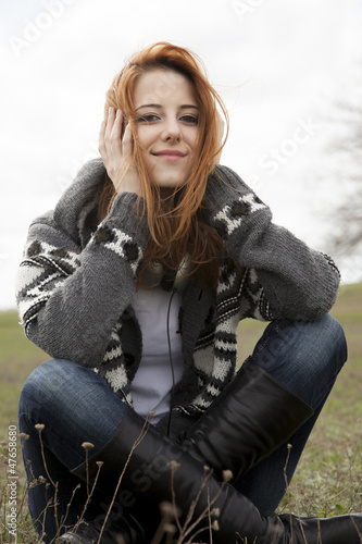 Photo: Young girl with headphones sitting at spring meadow. Young girl with headphones sitting at spring meadow.