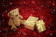 Teddy bear with golden gift box on red