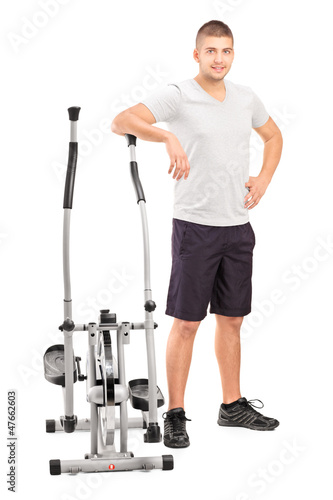 Photo: Male athlete standing next to a cross trainer machine Male athlete standing next to a cross trainer machine