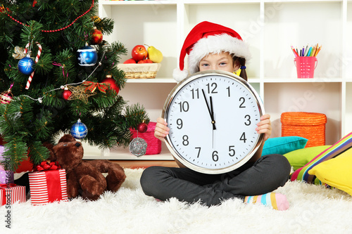 Photo: Little girl holding clock near christmas tree Little girl holding clock near christmas tree