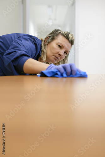 Photo: Professional female cleaner wiping table in office Professional female cleaner wiping table in office
