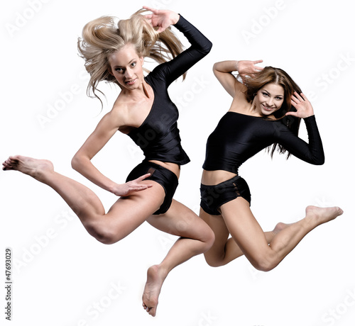 Photo: Two beautiful athletic girl jumping over white background Two beautiful athletic girl jumping over white background
