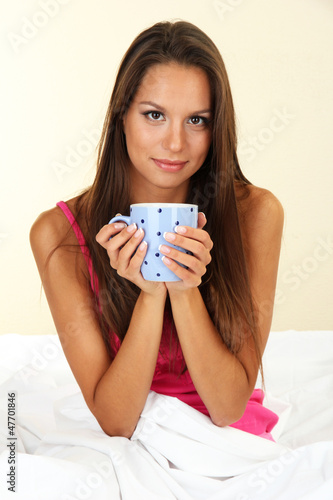 Photo: young beautiful woman with cup in bed young beautiful woman with cup in bed