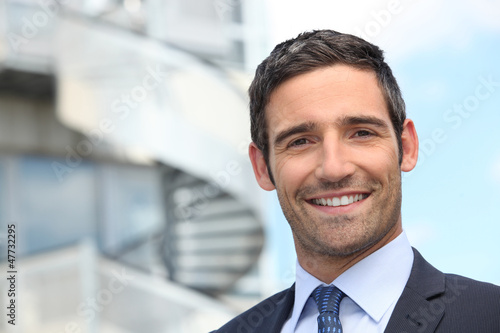 Photo: Smiling business man standing outside office building Smiling business man standing outside office building