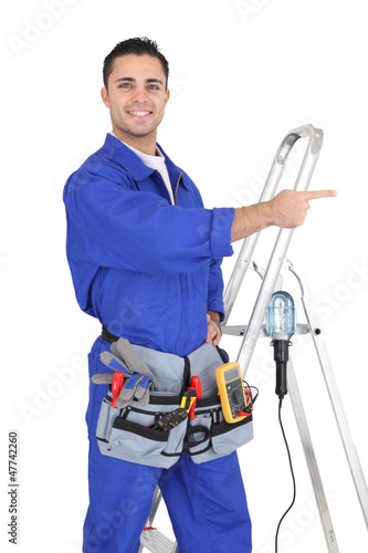 Photo: Electrician stood by his equipment pointing Electrician stood by his equipment pointing