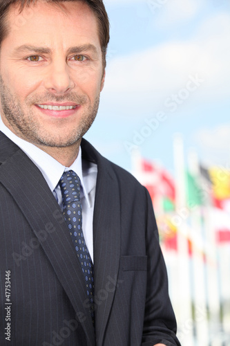 Photo: Businessman standing in front of international flags Businessman standing in front of international flags