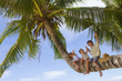 three children - boy and girls - sitting on palm tree on tropica