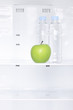 A green apple and bottles of water in a fridge