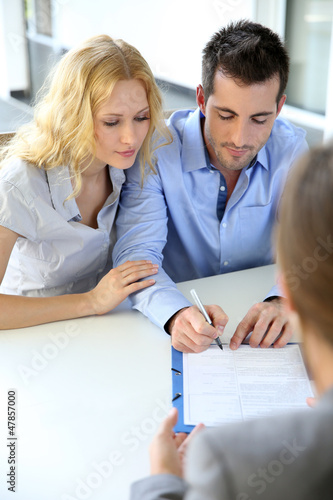 Photo: Cheerful couple signing property contract with real-estate agent Cheerful couple signing property contract with real-estate agent