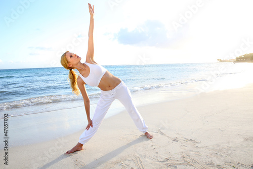Photo: Beautiful woman doing yoga exercises by the beach Beautiful woman doing yoga exercises by the beach