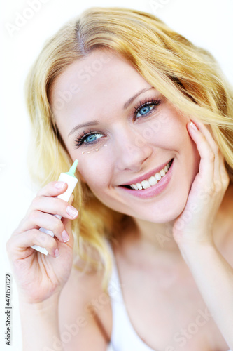 Photo: Smiling woman applying concealer in front of mirror Smiling woman applying concealer in front of mirror