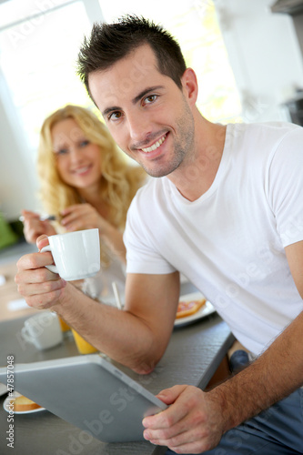 Photo: Young man sitting in home kitchen with tablet Young man sitting in home kitchen with tablet