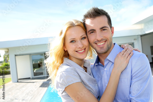 Photo: Cheerful couple standing in front of modern house Cheerful couple standing in front of modern house