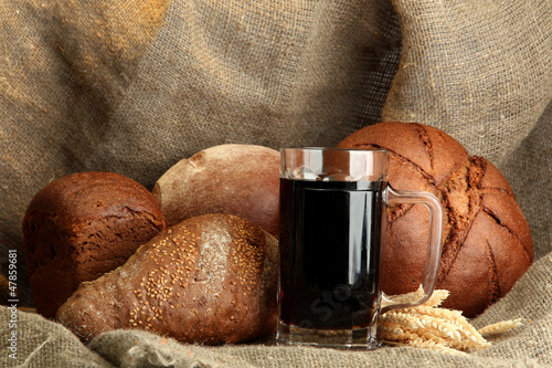 Photo: tankard of kvass and rye breads with ears, on burlap background tankard of kvass and rye breads with ears, on burlap background