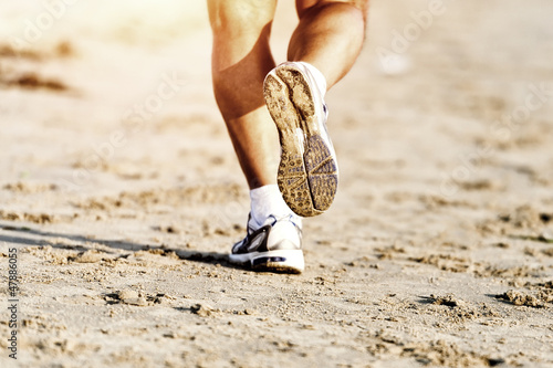 Photo: Runner feet running on beach closeup on shoe Runner feet running on beach closeup on shoe