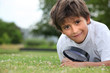 Boy with magnifying glass lying on the grass