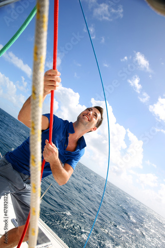 Photo: Young man lifting the sail of catamaran during cruising Young man lifting the sail of catamaran during cruising