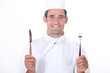 Chef in uniform holding a knife and fork