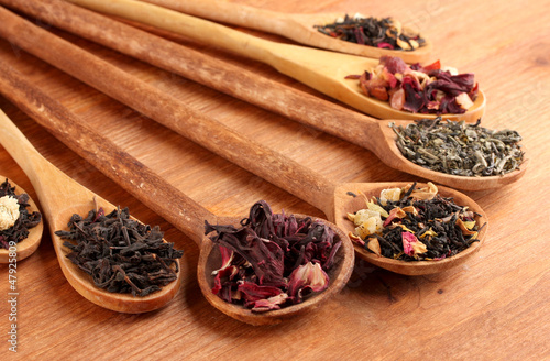 Photo: assortment of dry tea in spoons, on wooden background assortment of dry tea in spoons, on wooden background