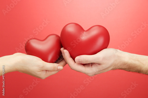 Photo: Red hearts in woman and man hands, on red background Red hearts in woman and man hands, on red background