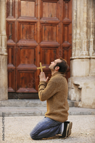 Photo: Man praying in front of the church holding a cross Man praying in front of the church holding a cross