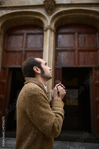 Photo: Man praying in church holding prayer beads Man praying in church holding prayer beads