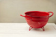 Red empty colander on white wooden table
