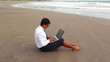 guy in office suit printing on laptop sitting on the beach