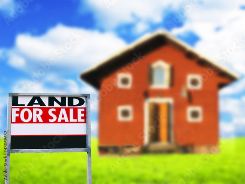 Photo: "LAND FOR SALE" sign against wooden house - Real estate concept "LAND FOR SALE" sign against wooden house - Real estate concept