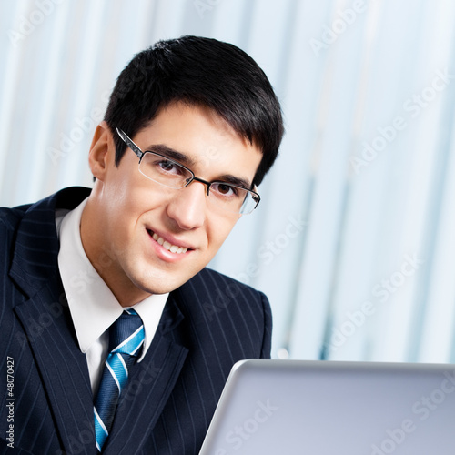 Photo: Smiling businessman working with laptop at office Smiling businessman working with laptop at office