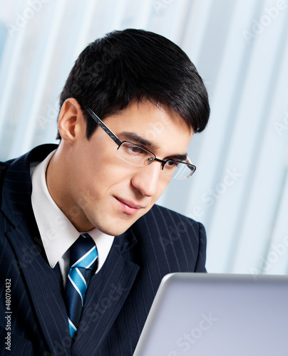 Photo: Smiling businessman working with laptop at office Smiling businessman working with laptop at office