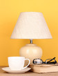 table lamp with cup, book and glasses on yellow background
